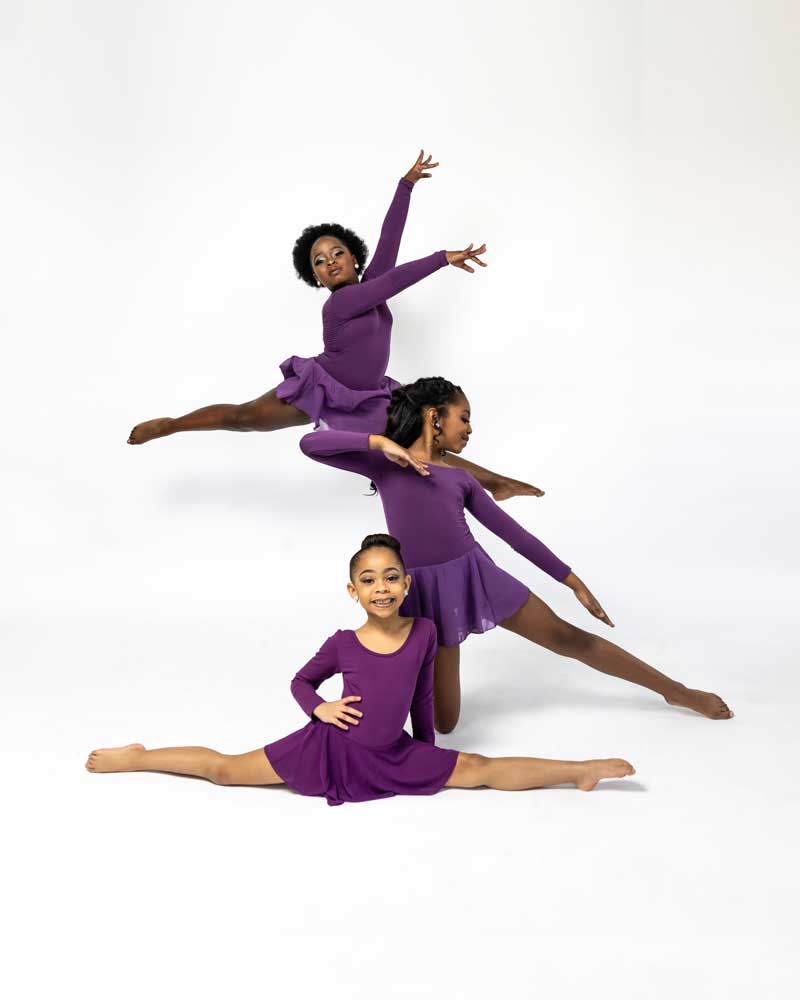 Three young Dance ELITE dancers in purple leotards holding a split pose